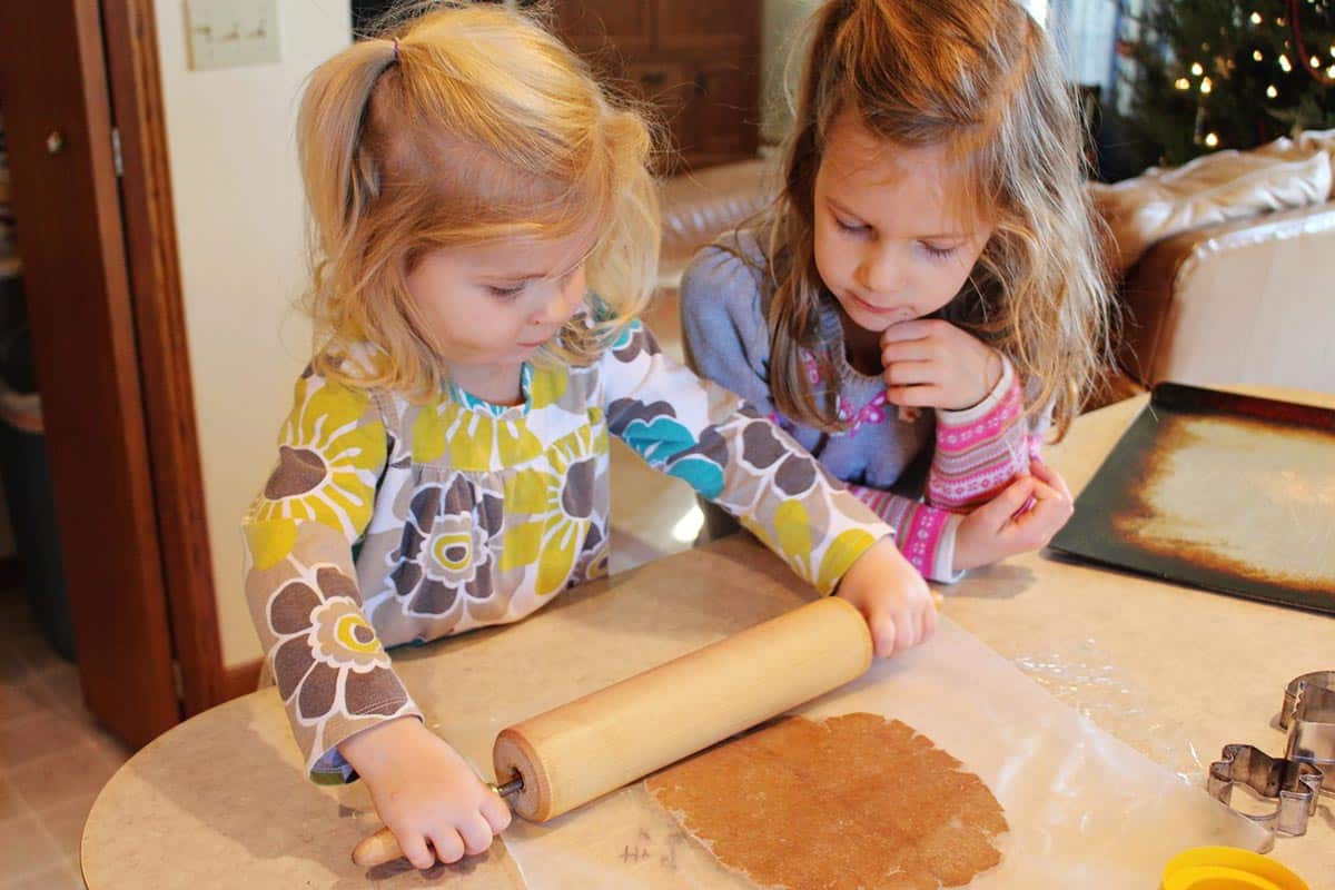 Two children using a rolling pin to roll out gingerbread cookie dough.