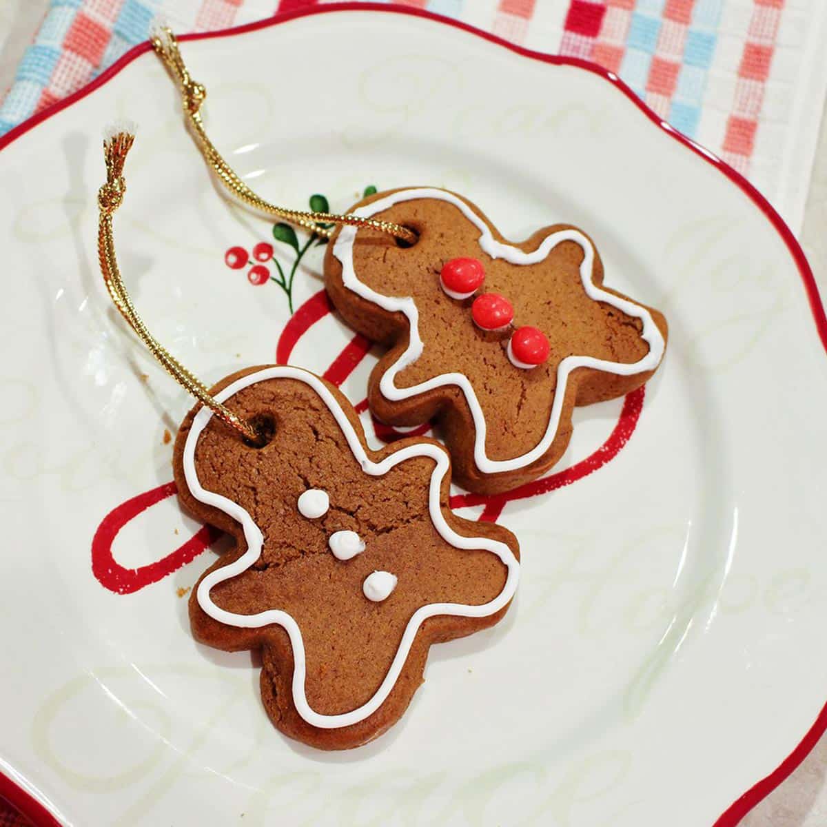 Two gingerbread ornaments decorated with red hots and white icing, sitting on a Christmas plate.