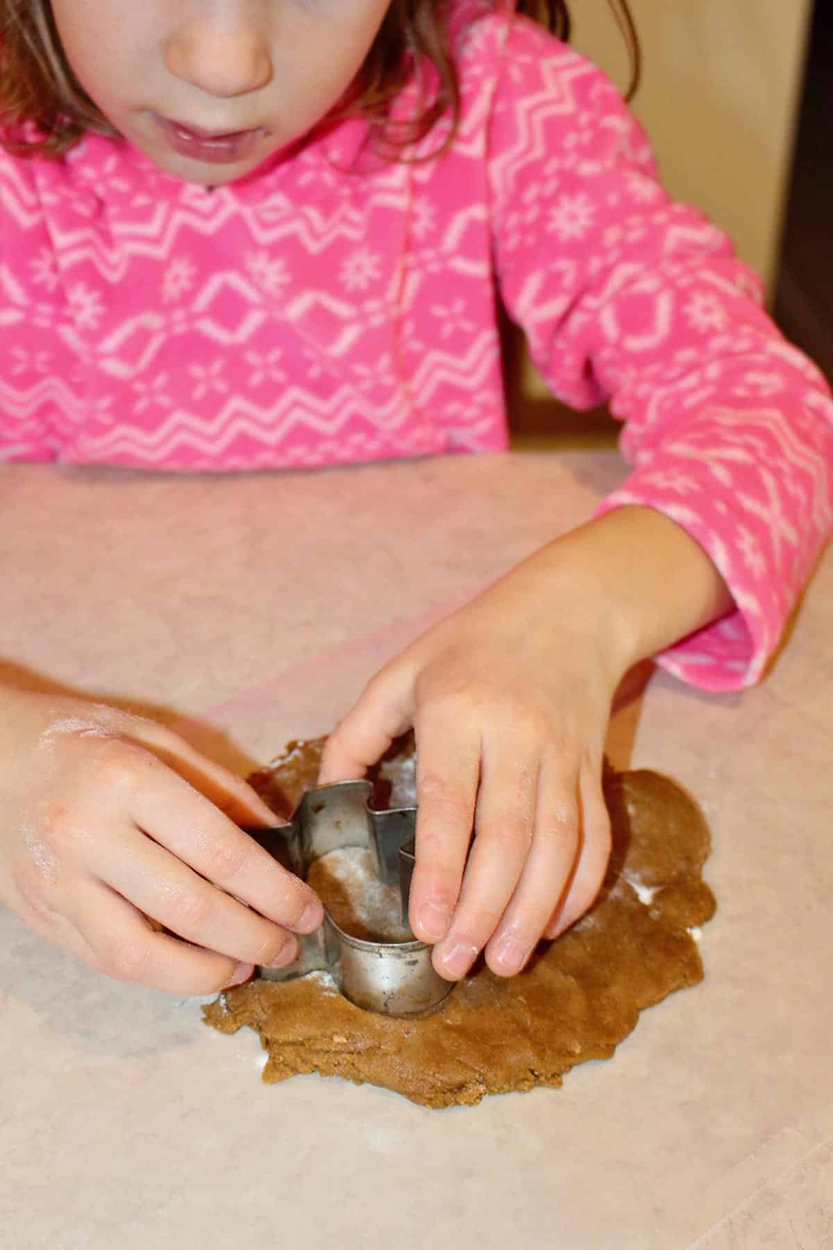 A child using a cookie cutter to cut a gingerbread man shape from cookie dough