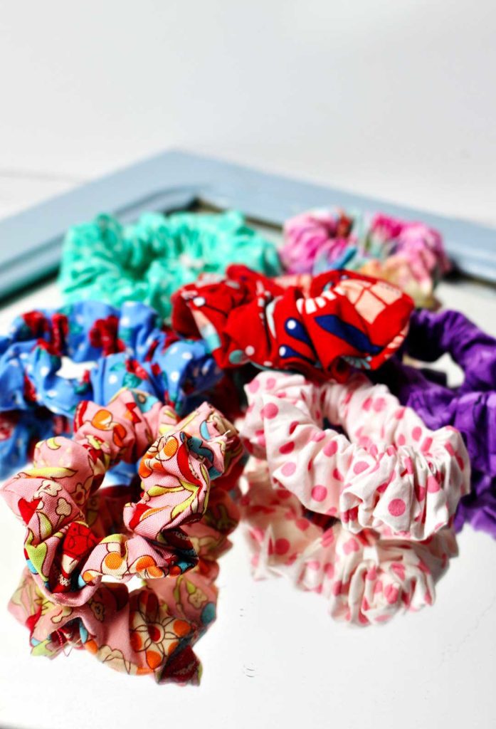 A mirror laying flat with seven scrunchies made from bright patterned fabrics.