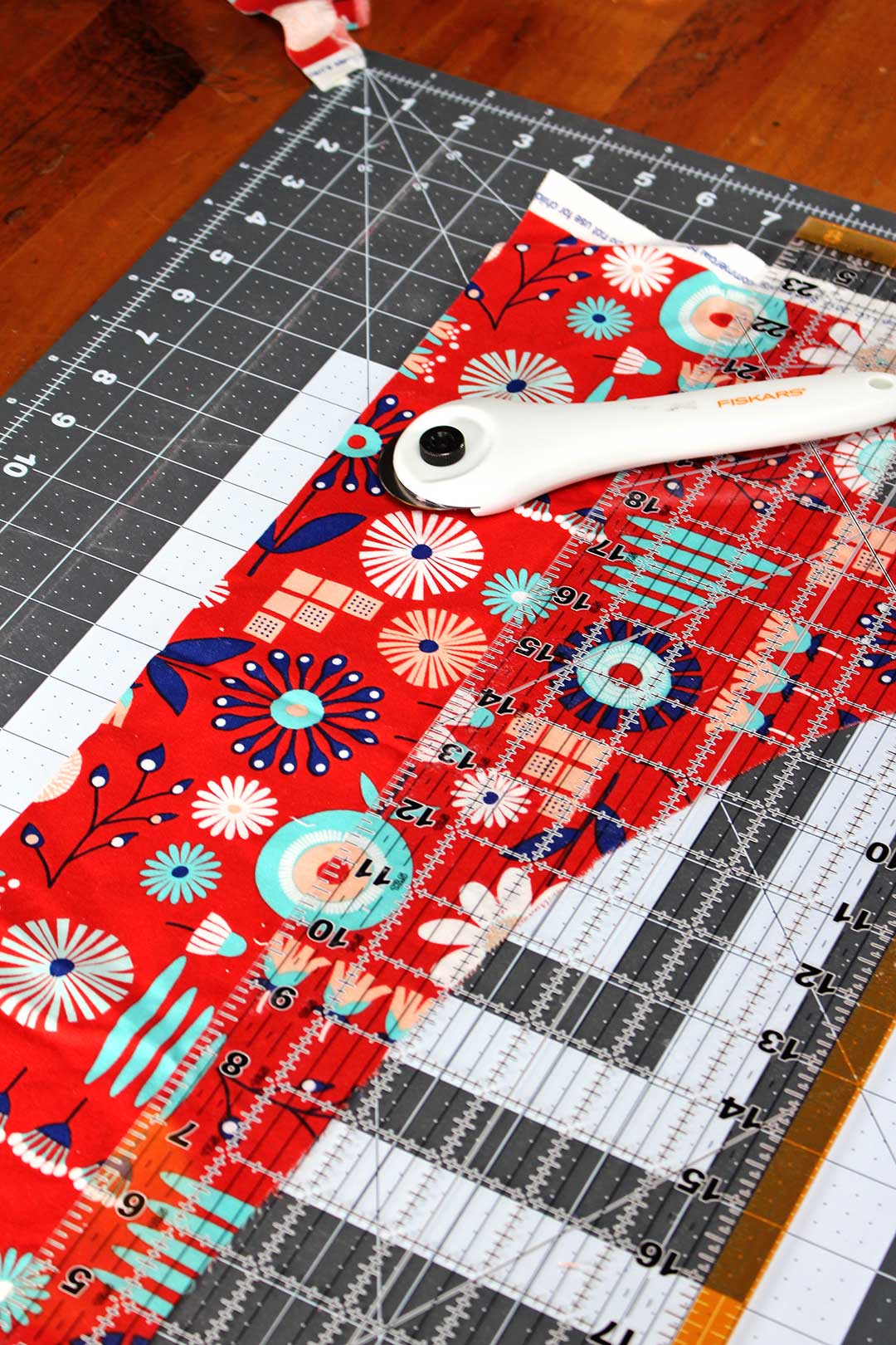 Cutting mat, red and blue patterned fabric, clear ruler and rotary cutter.
