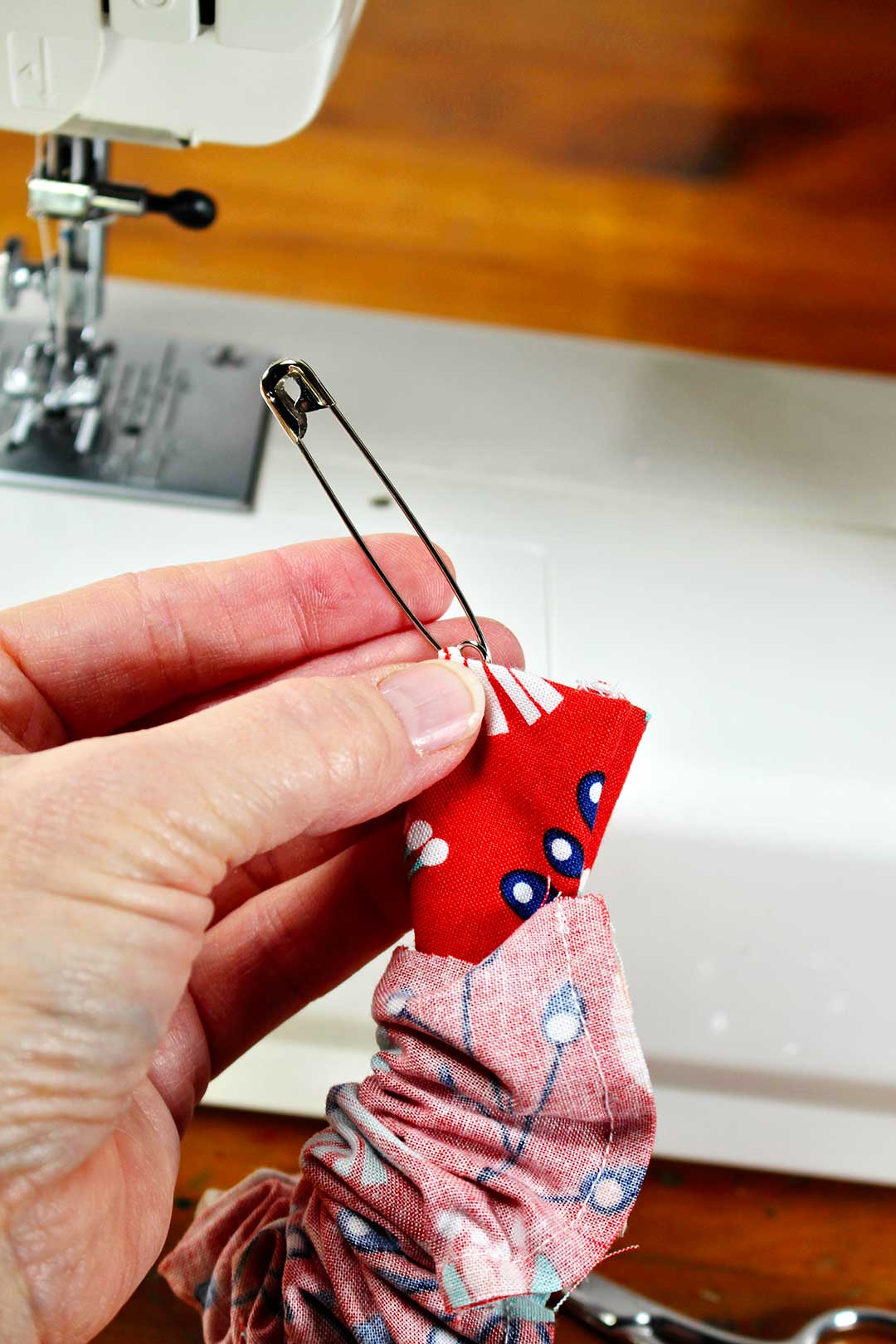 Person holding partially made scrunchie with safety pin threading the elastic through the fabric.