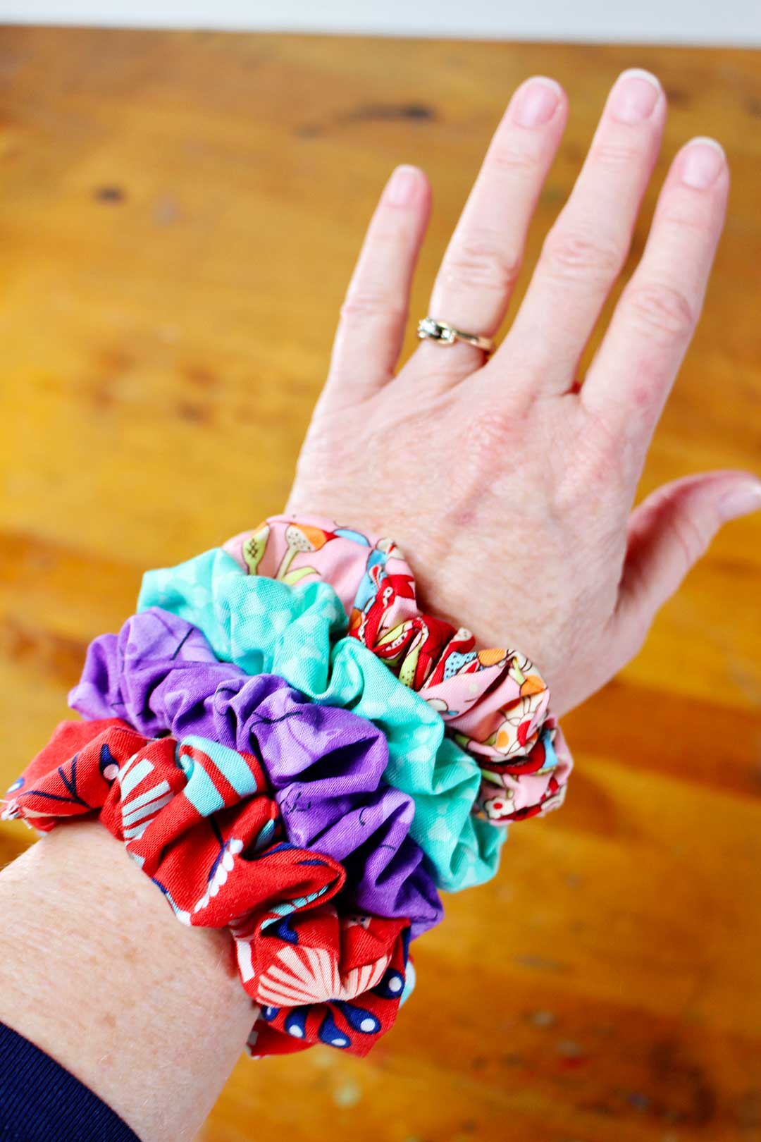 Woman's wrist displayed with four different colorful homemade scrunchies.