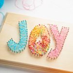 Close up shot of finished "joy" string art in blue, pink and multi colored string.