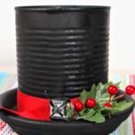 DIY Frost the Snowman Hat Candle made from black painted can decorated with holly, red ribbon and bell.