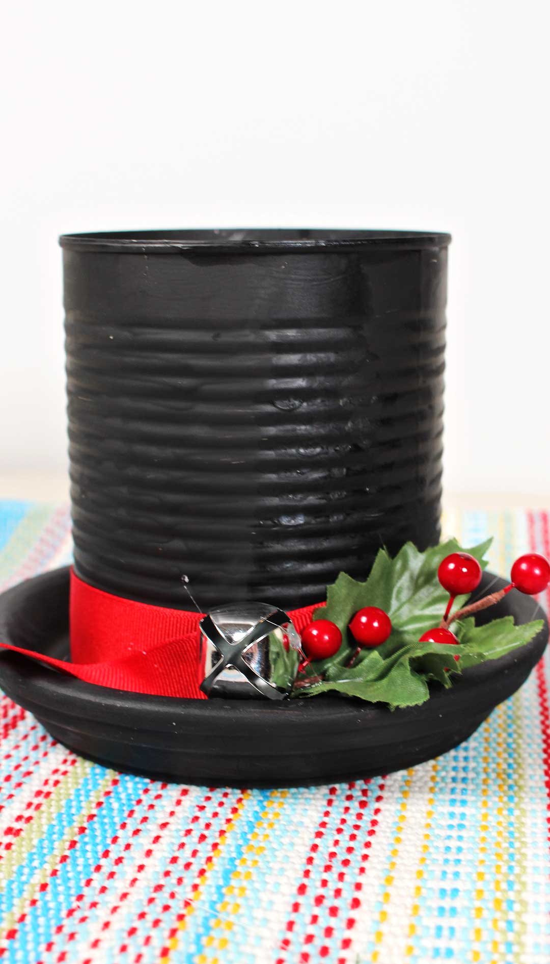 DIY Frost the Snowman Hat Candle made from black painted can decorated with holly, red ribbon and bell.