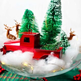 Closer view of the inside of the glass bowl centerpiece with old fashion red truck, faux trees, plastic deer, cotton "snow" and LED lights.