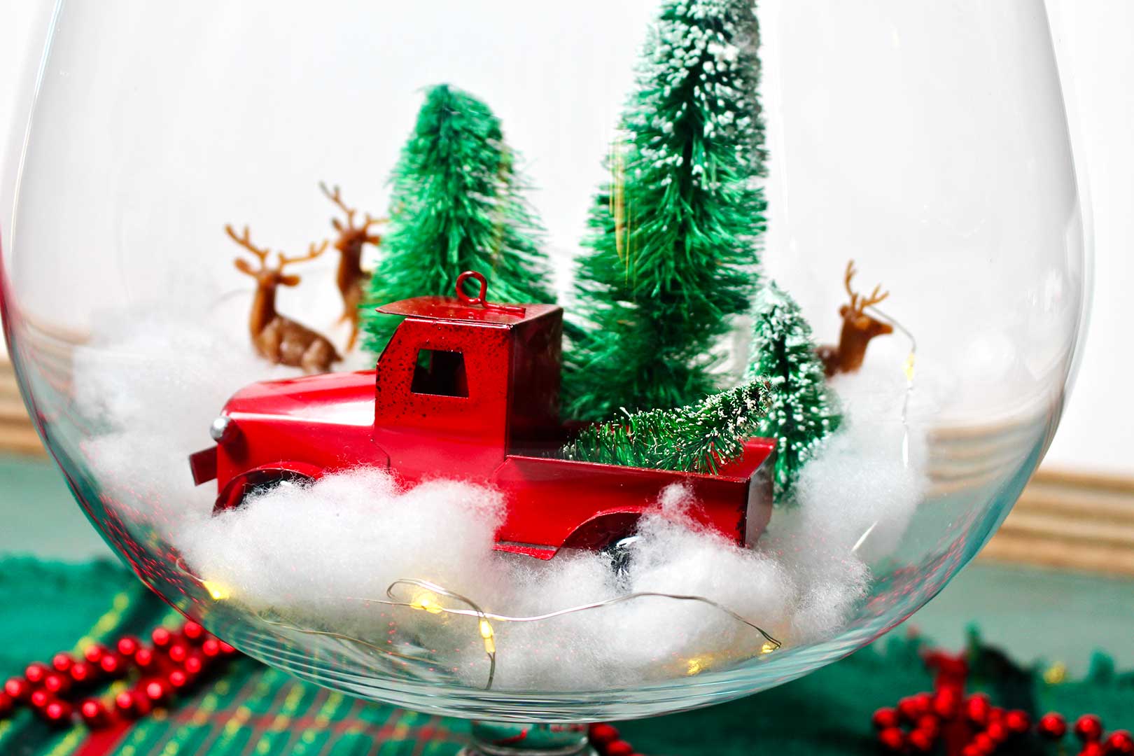 Closer view of the inside of the glass bowl centerpiece with old fashion red truck, faux trees, plastic deer, cotton "snow" and LED lights.