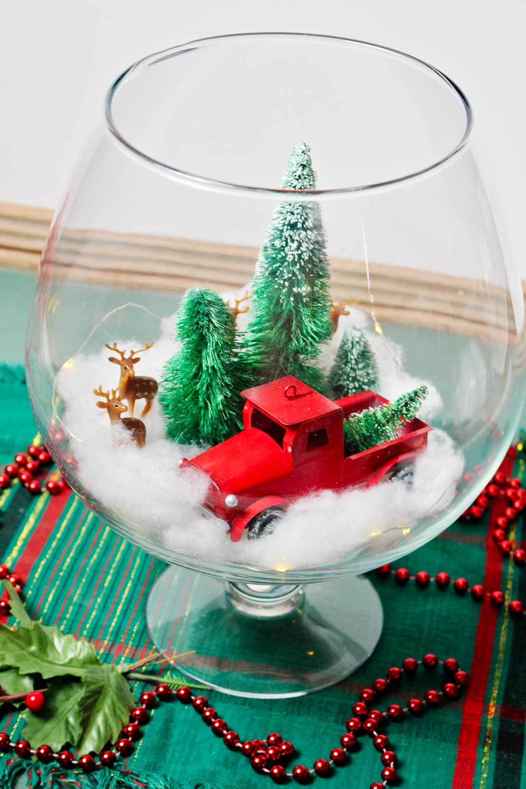 Finished image of glass bowl Christmas centerpiece resting on table with green plaid runner and red beaded garland.