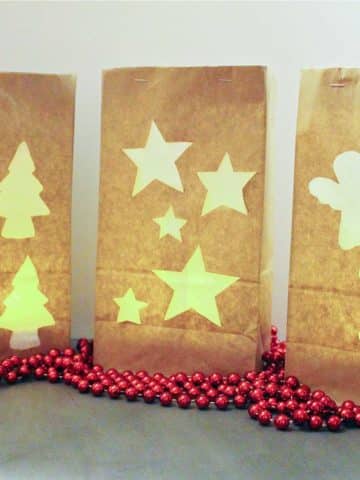 Three brown paper bags with Christmas shapes cut out, glowing from a candle inside