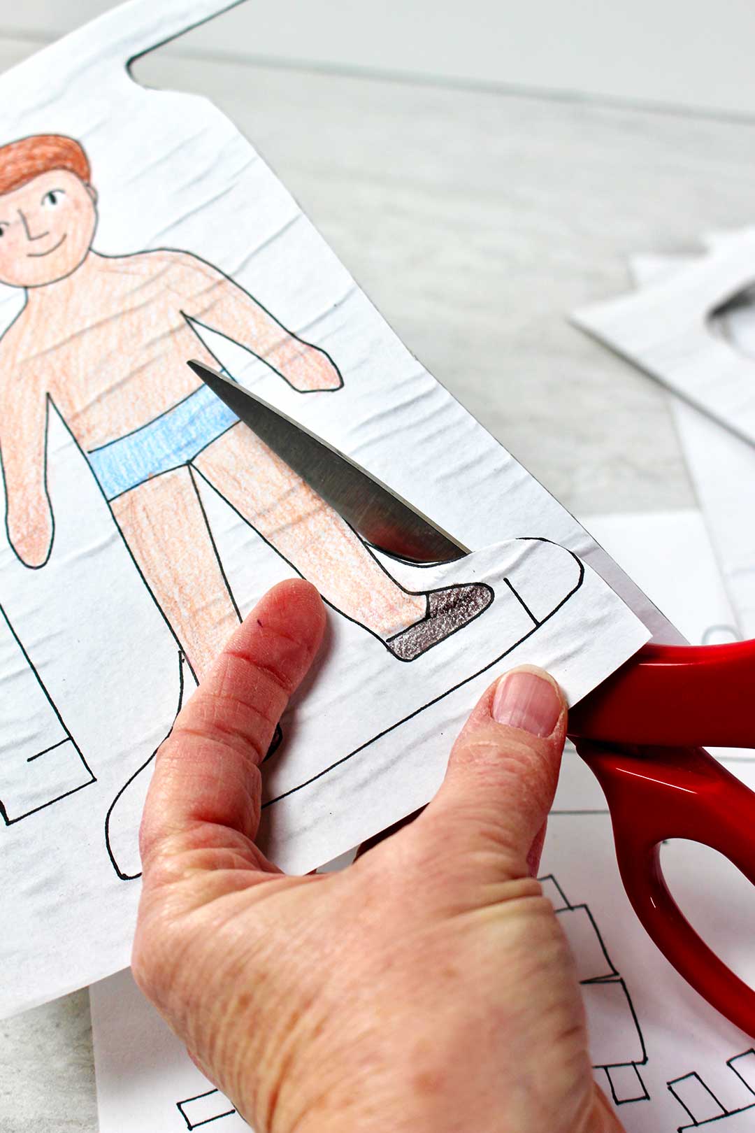 Person cutting out male paper doll with red scissors.