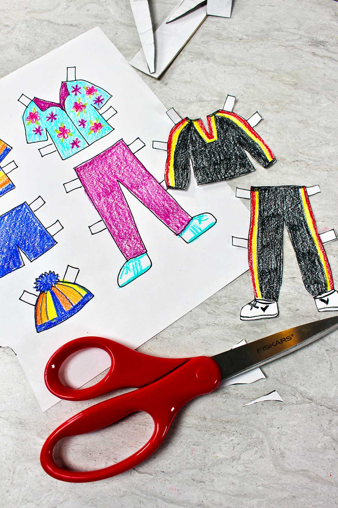 Different colored outfits for paper dolls, some cut out and some on sheet. Red scissors nearby.