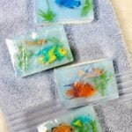 Four completed soaps, packaged in plastic wrap resting on a blue bath towel.
