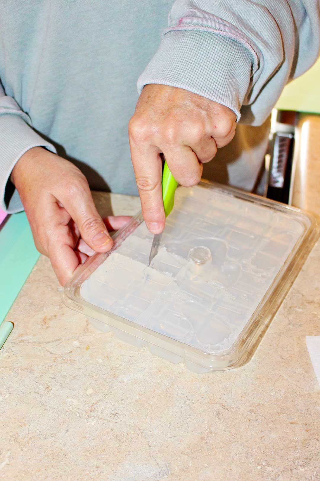 Woman slicing through block bulk clear soap with bright green knife.