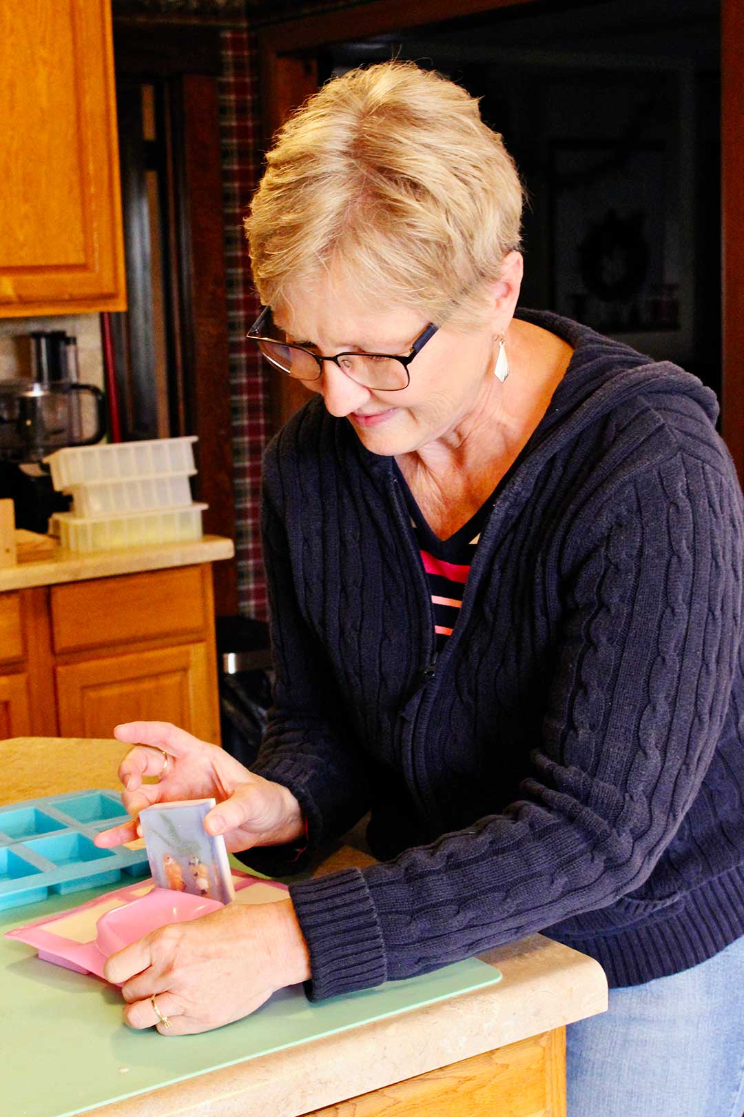 Woman peeling hardened soap out of pink silicone soap mold in kitchen.