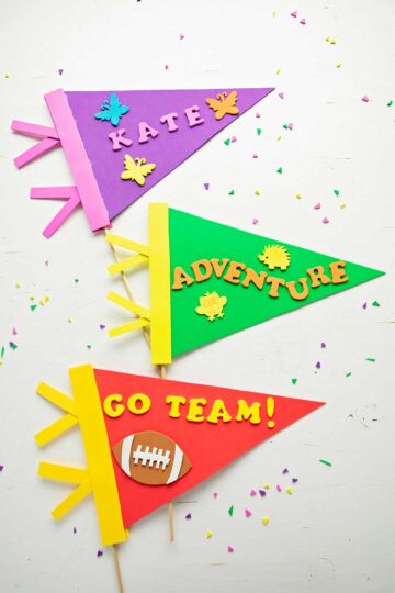 Three finished pennants. One purple, one green and one red with foam letters and shapes decorating them.