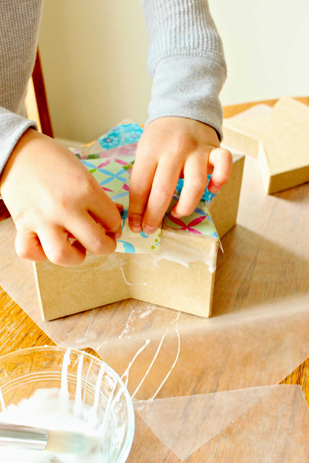 Close up view of child's hands pressing some colorful paper onto places where she painted Mod Podge onto her star shaped box.