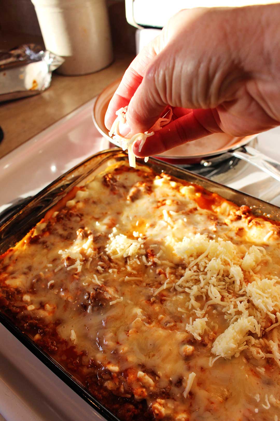 Person sprinkling shredded cheese on an almost finished pan of easy lasagna.