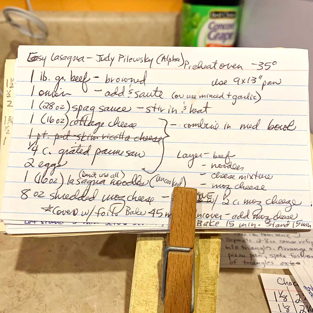 Hand written recipe for lasagna on an index card being held up to the camera by a clothes pin.