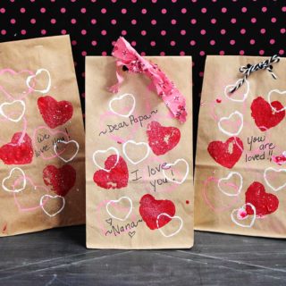 Three completed treat bags decorated with pink, red and white hearts, ribbon and cute note with polka dot background.