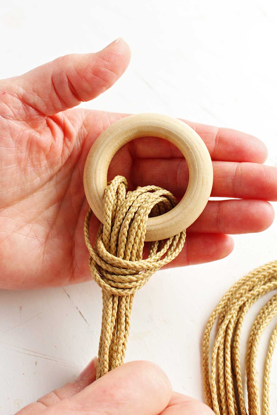 Close up view of wooden ring and first loop of bundled rope for macrame hanger.