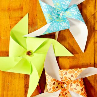 Three finished colored pattern paper pinwheels on a wooden table. (vertical image)