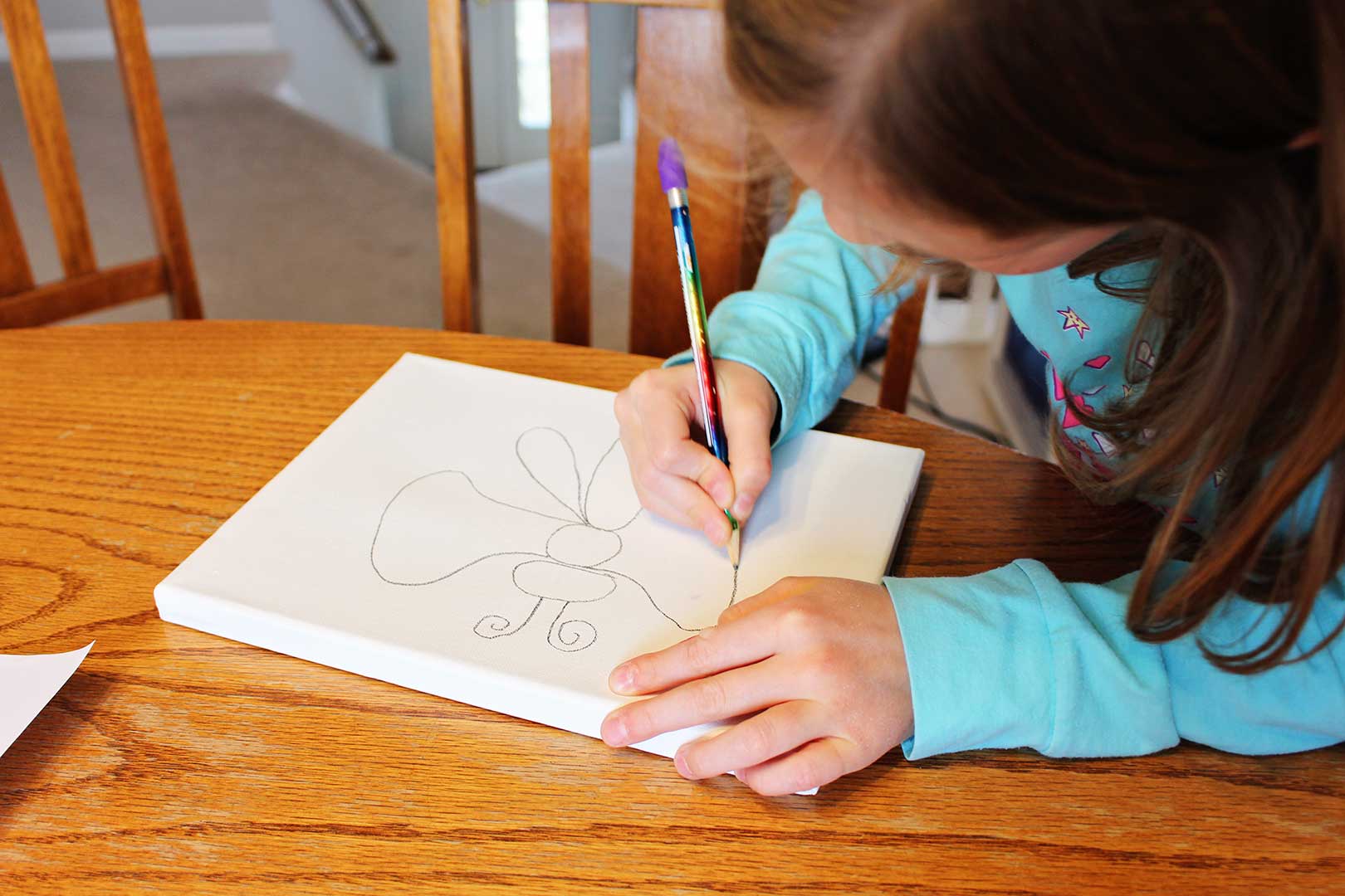 Fille dessinant un dessin de papillon avec un crayon sur une toile blanche.