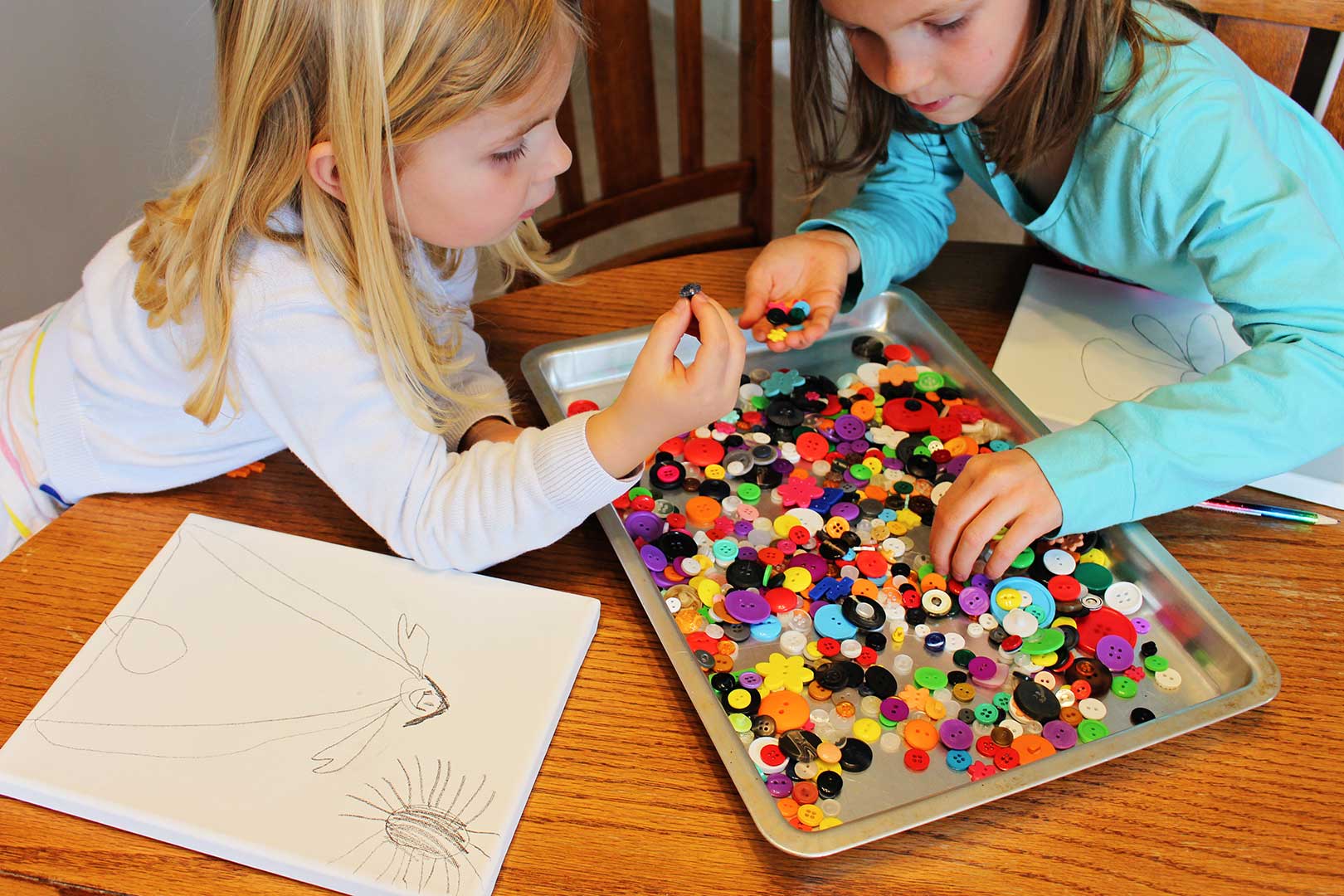 Deux jeunes filles à la recherche de boutons multicolores dans une plaque à biscuits pour leur dessin sur toile.