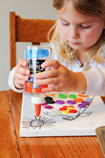 Blonde girl uses clear Elmer's glue on a drawing of a sunshine on her white canvas.