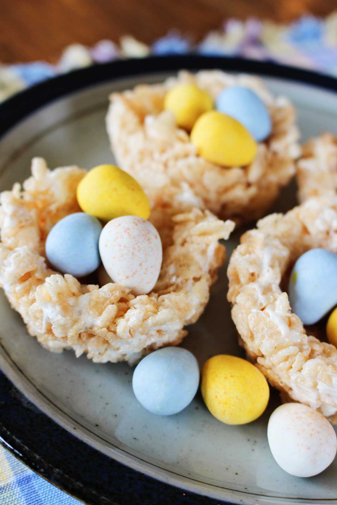 Several Rice Krispie Easter Nests with chocolate eggs inside sitting on a plate.