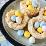 Several Rice Krispie Easter Nests with chocolate eggs inside sitting on a plate.