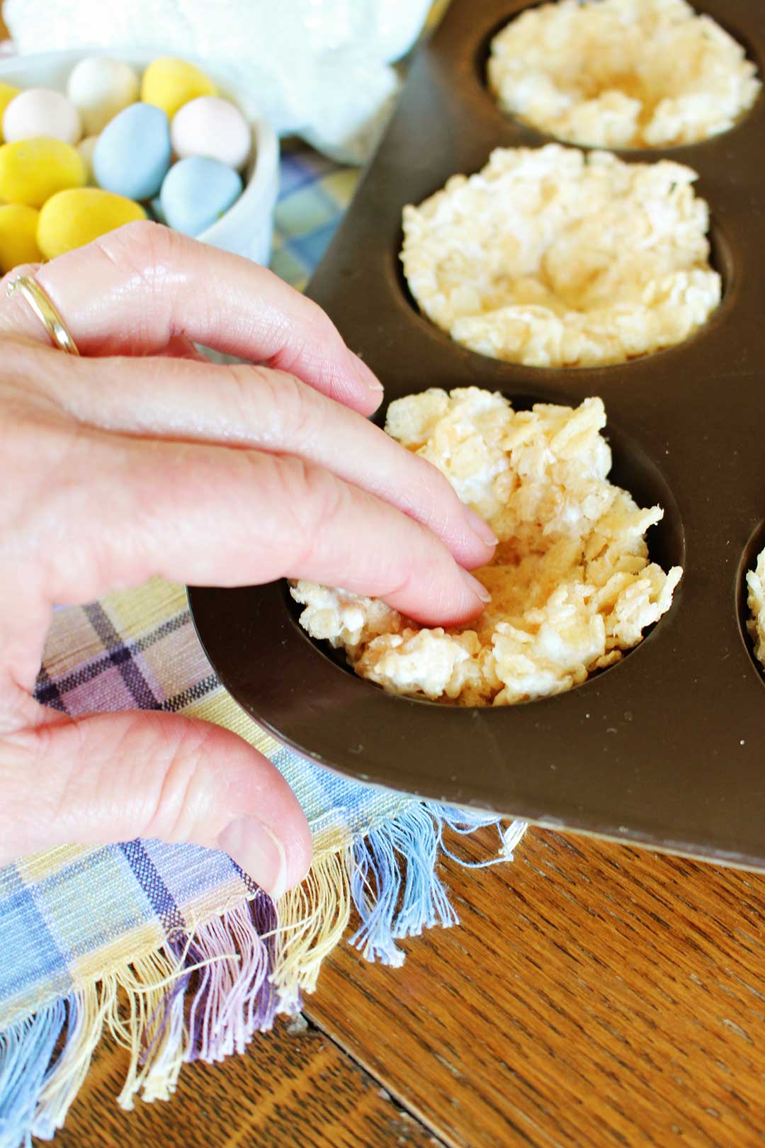 Fingers pressing rice krispie treats into the shape of a nest in a muffin cup.