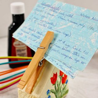 Completed recipe card holder painted with red tulips holds a blue recipe card in the clothes pin.