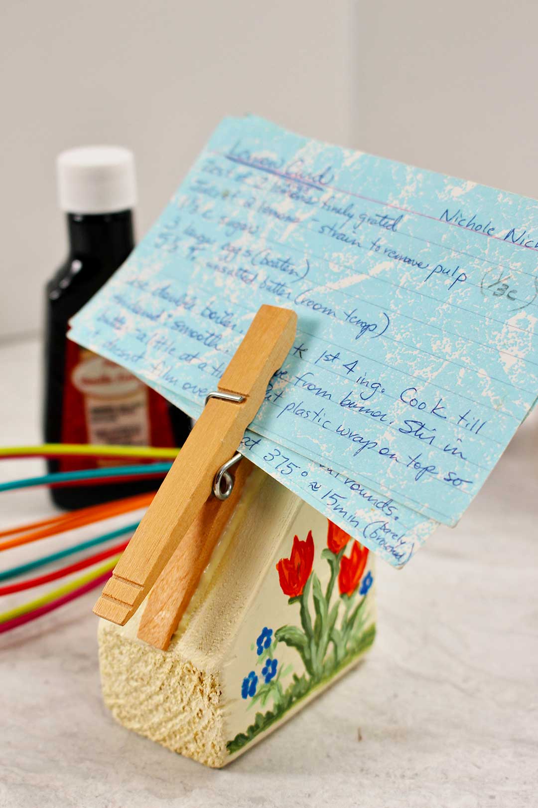 Completed recipe card holder painted with red tulips holds a blue recipe card in the clothes pin.