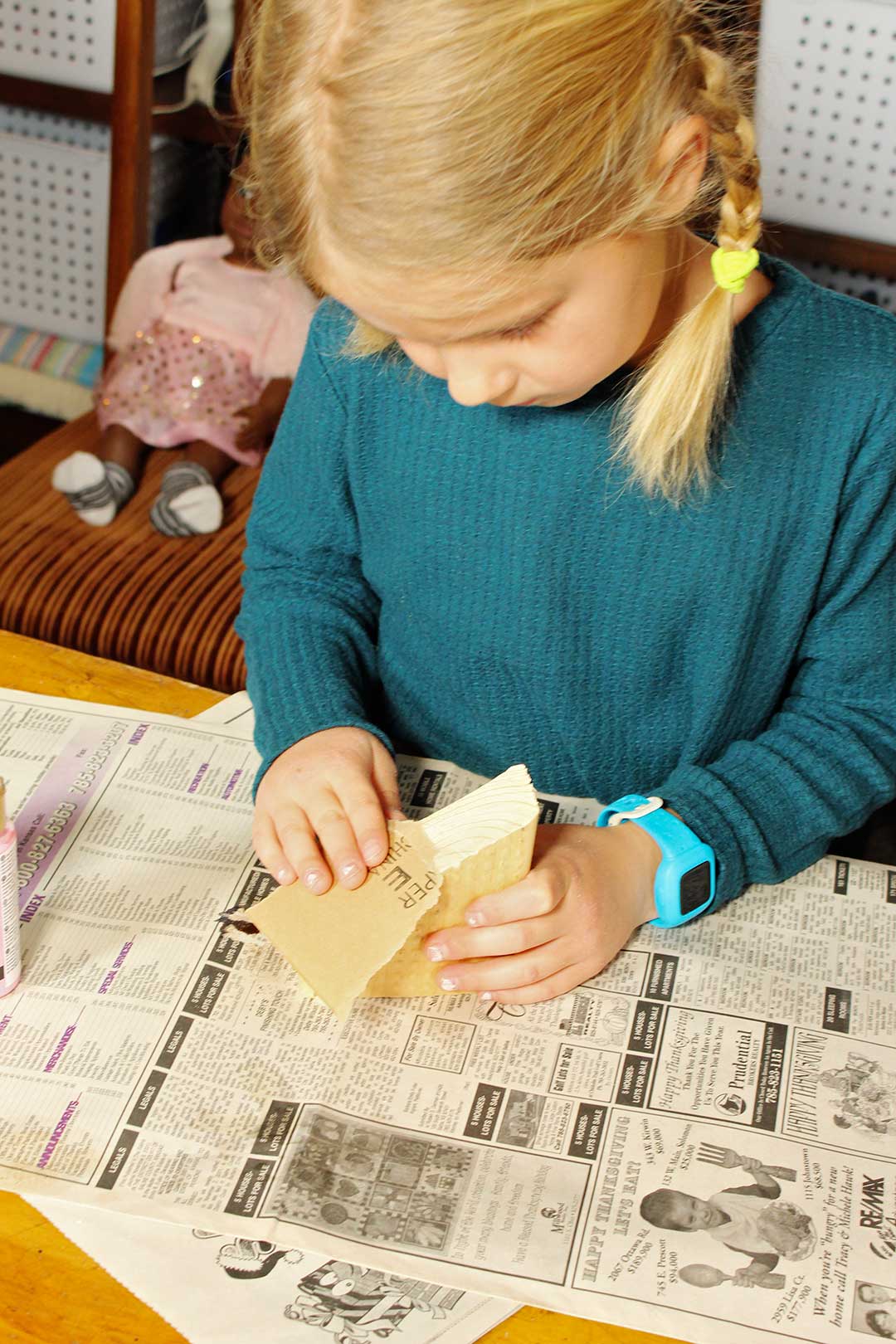 Young girl with blonde hair and pigtail braids sands her block of wood with sandpaper.