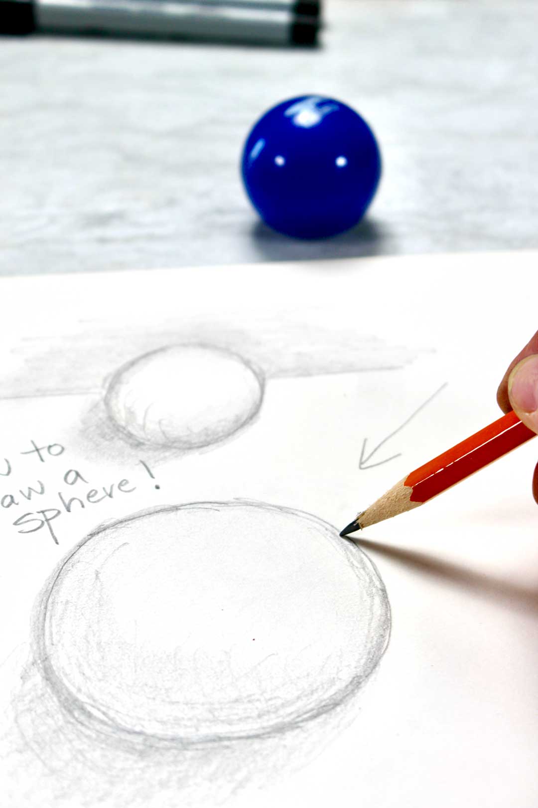 A pencil drawing the outline of a sphere, with a ball nearby.