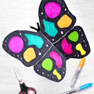 Artisanat de papillons en papier terminé coloré avec des fabricants de sharpie noir et néon reposant près d'une paire de ciseaux noirs et de marqueurs de sharpie néon.