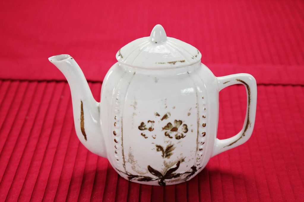 White antique child's tea pot on a red placemat