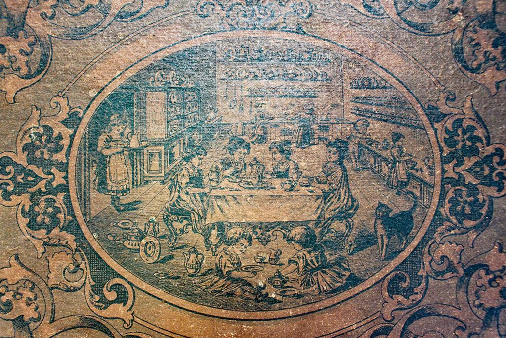 Cover of antique tea set box showing ladies having tea with children at their feet.