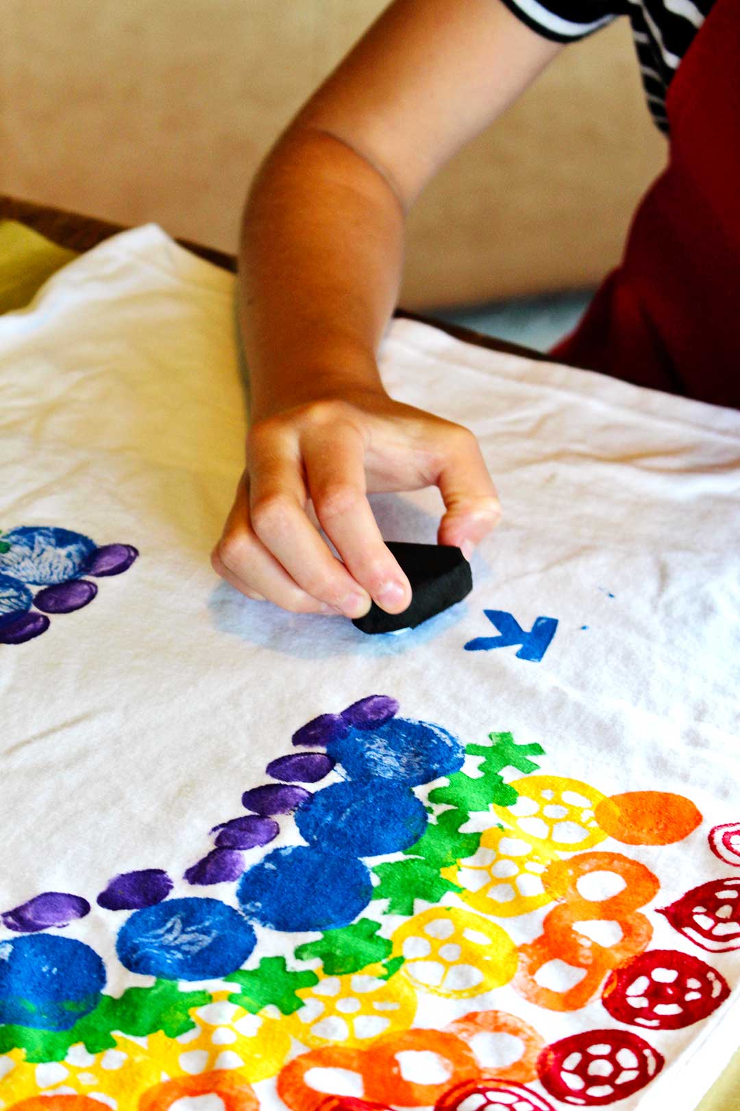 La main de l'enfant estampant des lettres bleues sur son T-shirt blanc.