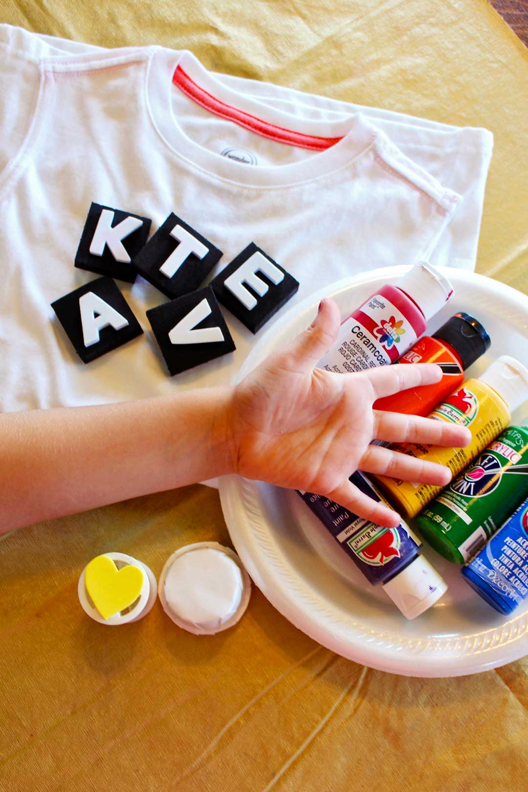 T-shirt blanc avec des tampons, de la peinture, des plaques de mousse et une main d'enfant tendue.