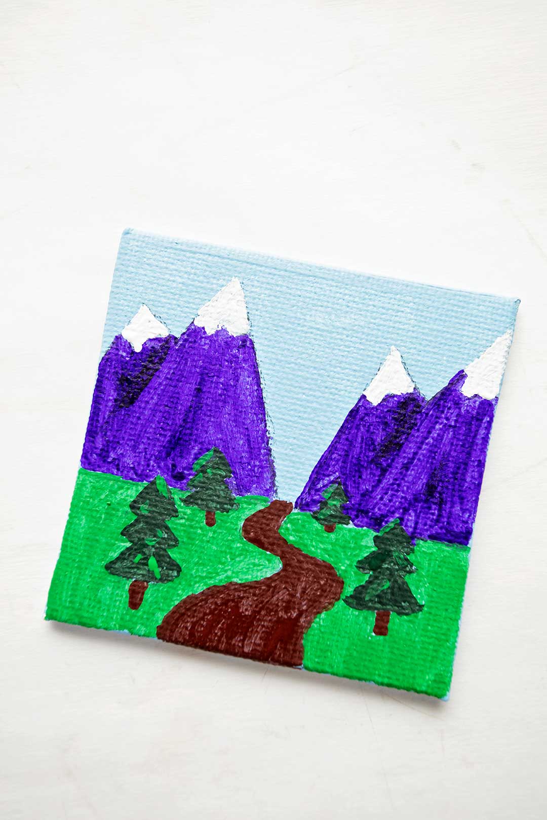 Finished mini canvas painting of purple mountains with trees and a trail.