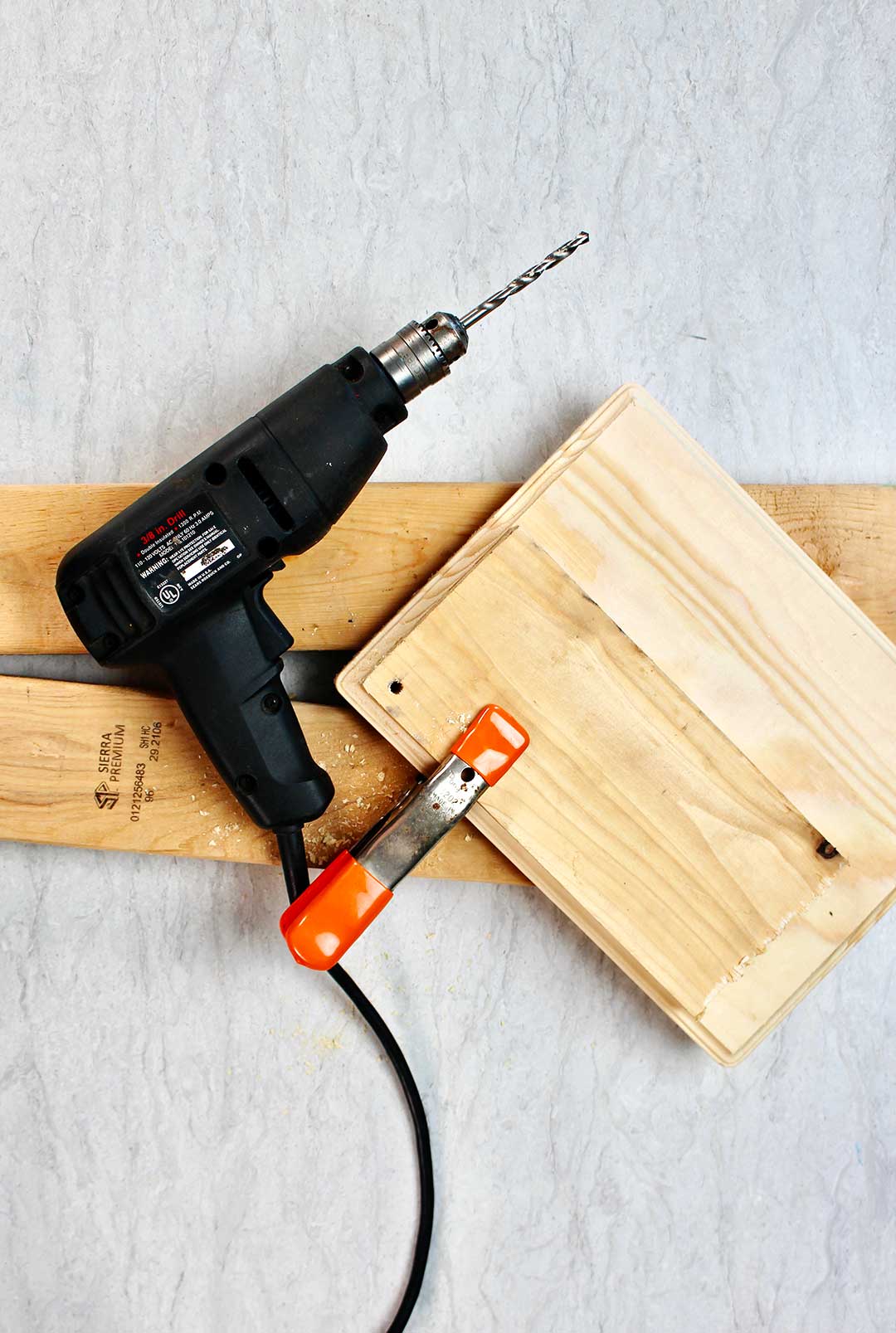 Black drill and orange clamp resting on pieces of wood.