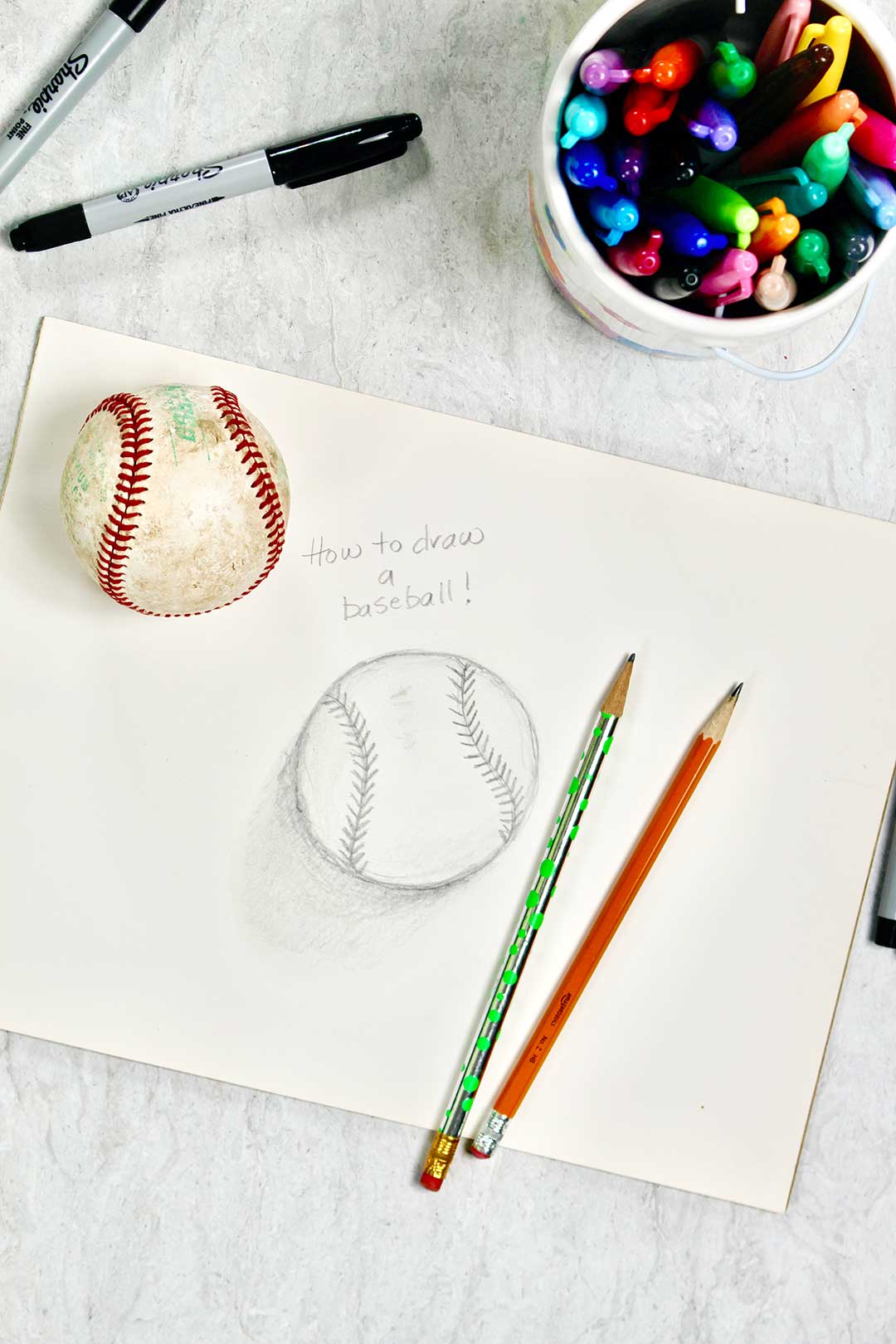 Final drawing of a baseball with sharpies, pencil and baseball nearby.
