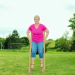 Nana smiling on stilts wearing bright pink shirt and jeans.