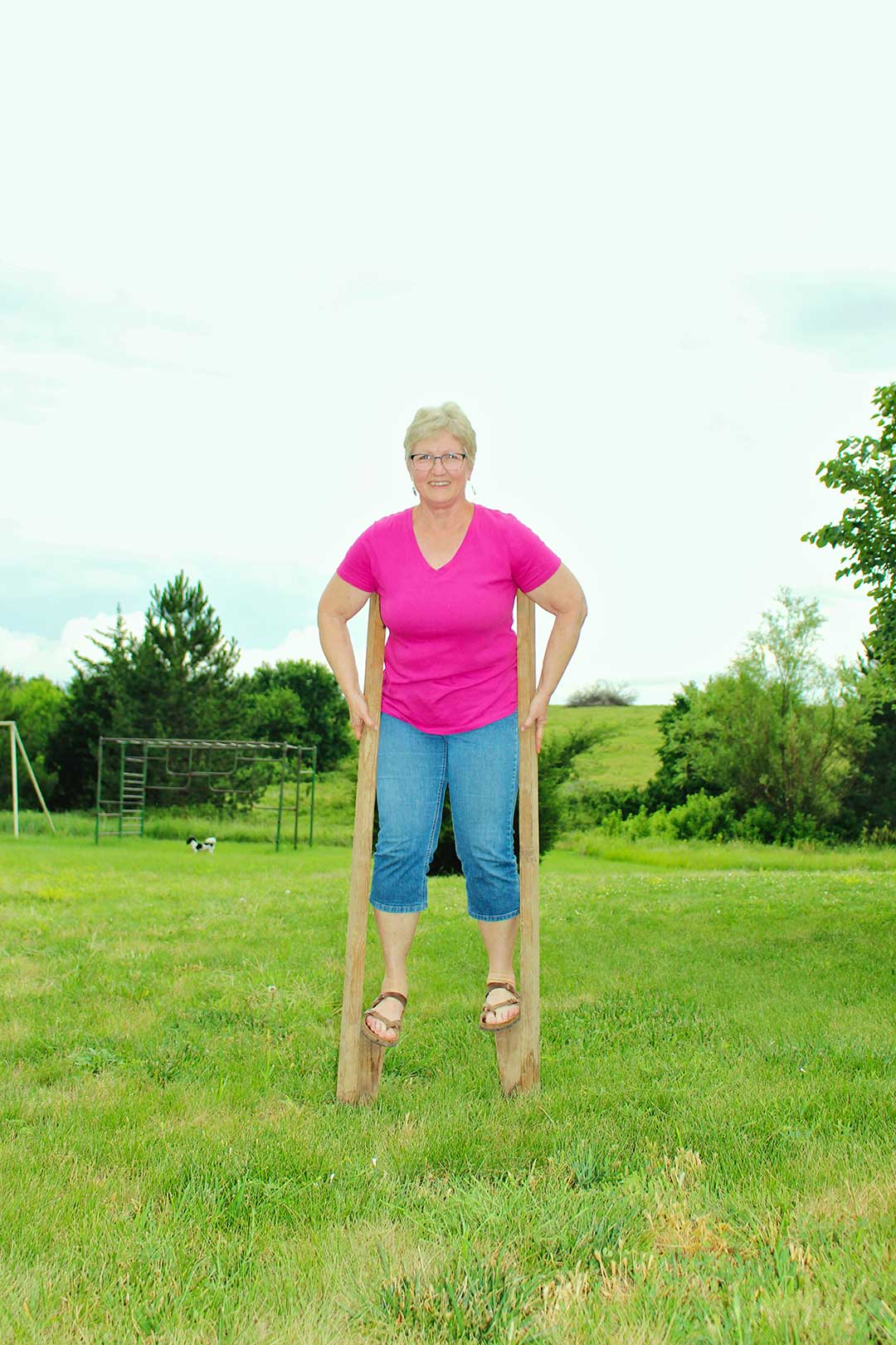 Nana smiling on stilts wearing bright pink shirt and jeans.