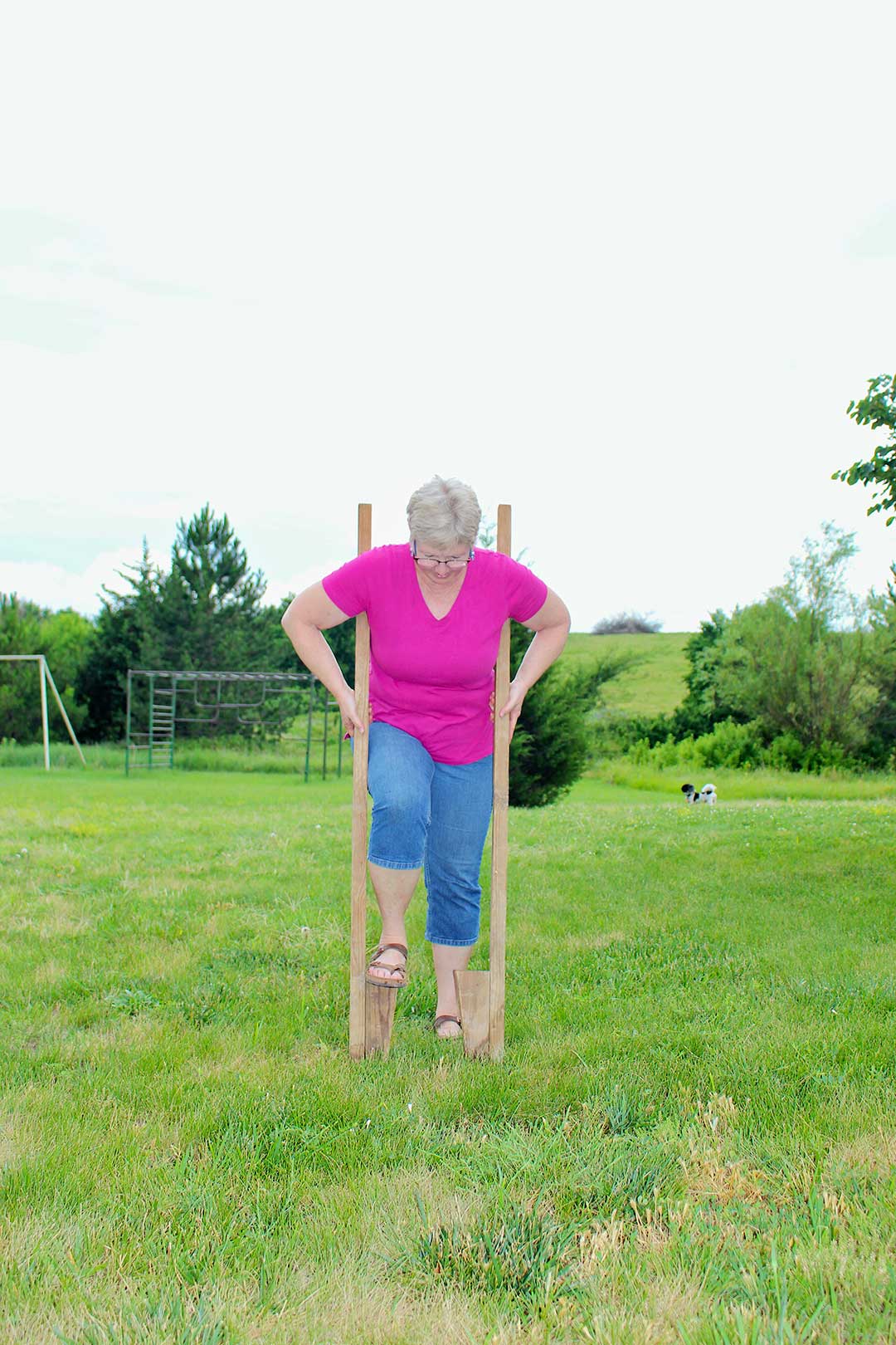 Nana getting up on stilts wearing a bright pink shirt and jeans.
