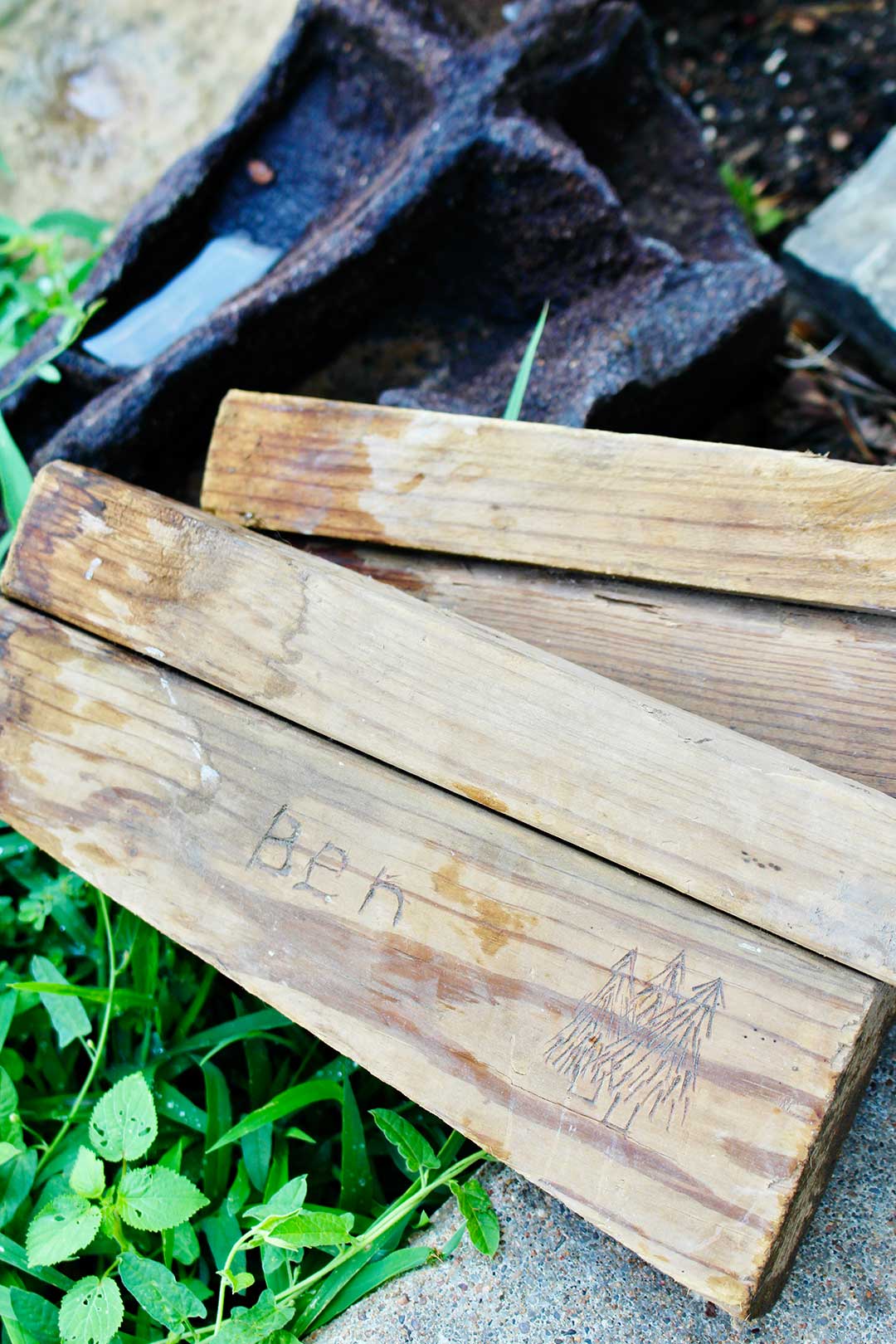 Spare wood pieces, one with the name "Ben" and evergreen trees burned into it.