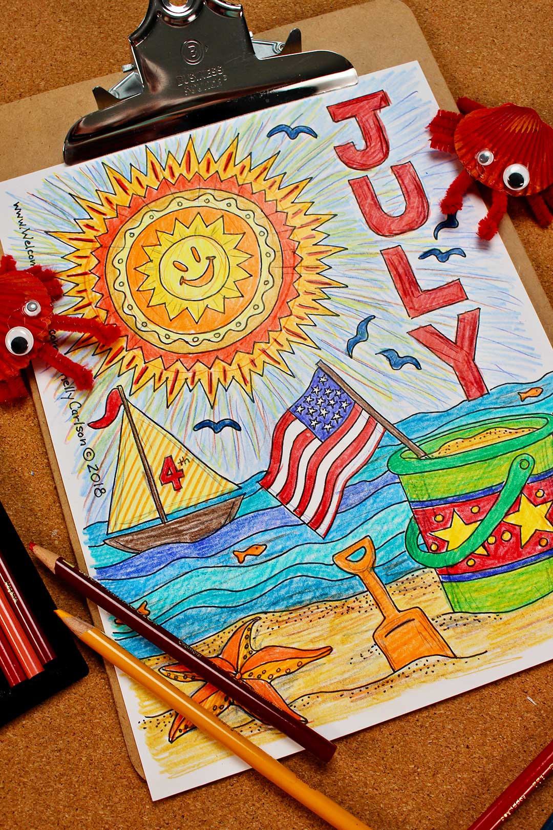 Finished July coloring page on clipboard with two DIY crabs and colored pencils near by.
