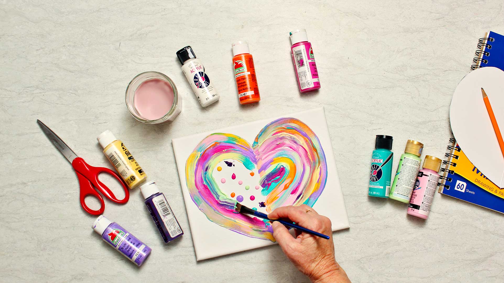 Overhead view of person painting abstract heart painting with painting supplies on a counter top.